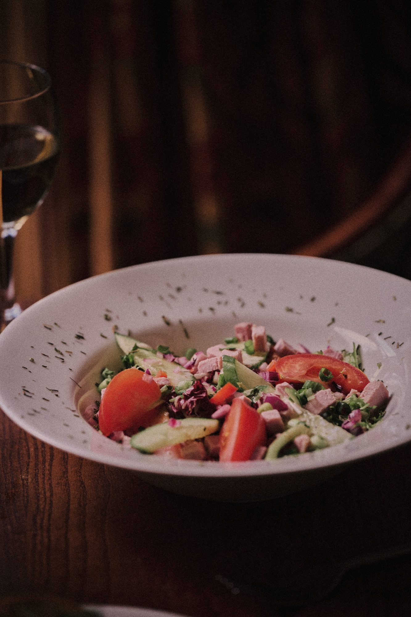 A dressed salad in a shallow bowl on a dark wood table at The Red Lion, a glass of wine behind.