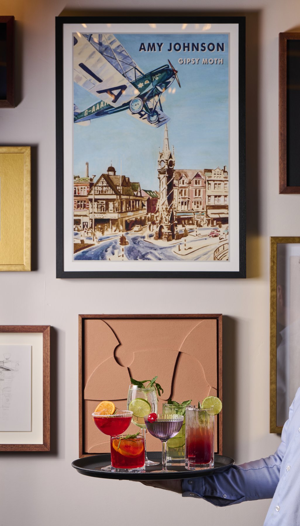 Framed prints on the wall at O.W. with a hand carrying a tray of drinks through the room.